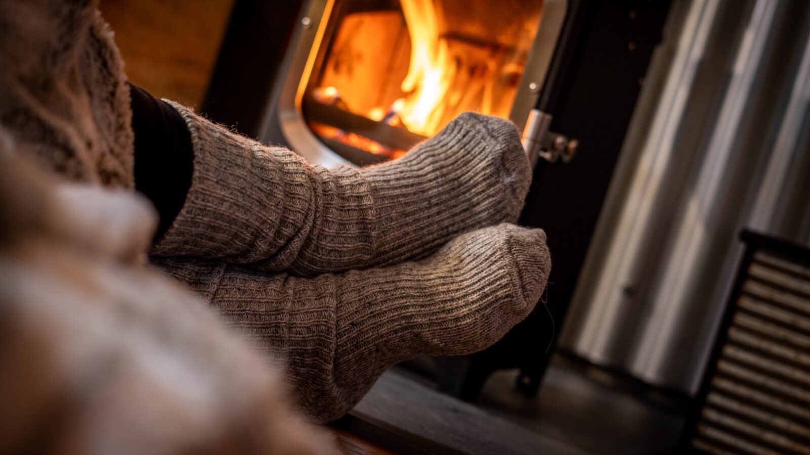 A cozy scene of a person wearing thick, gray wool socks while resting their feet near a warm, glowing fireplace at The Cabin. The focus is on the socks and the flames, creating a sense of warmth and comfort in this serene Erwain Escape.