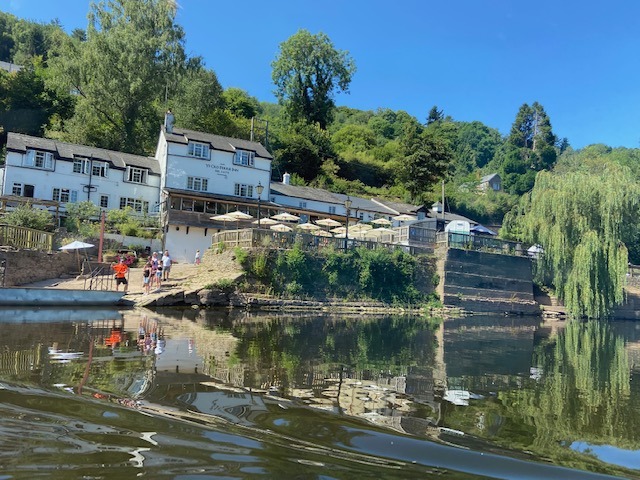 A riverside scene features a group of people gathered near the water in front of a white building labeled 