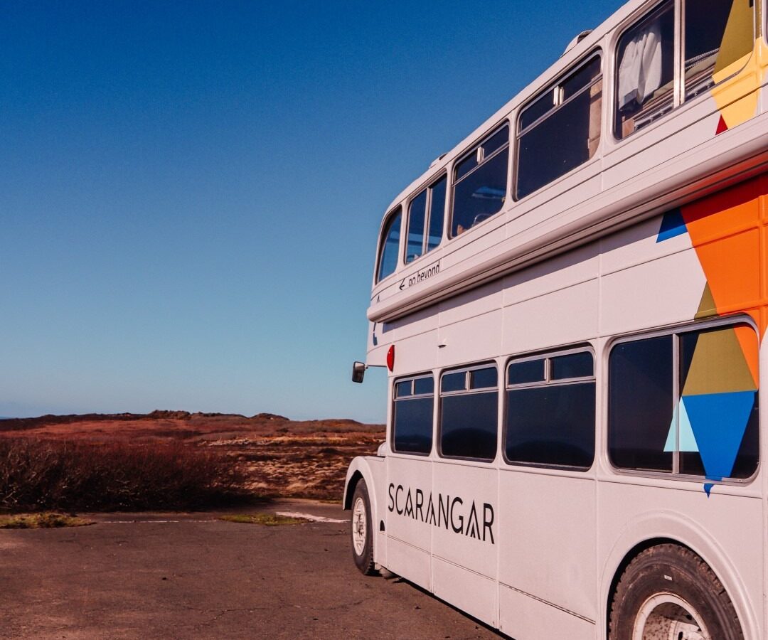 A white double-decker bus with colorful geometric shapes on its side and the word 