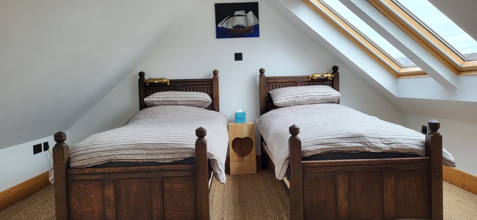 A cozy bedroom with two wooden twin beds, each with striped bedding. A small wooden nightstand with a heart cutout and a blue bottle labeled 